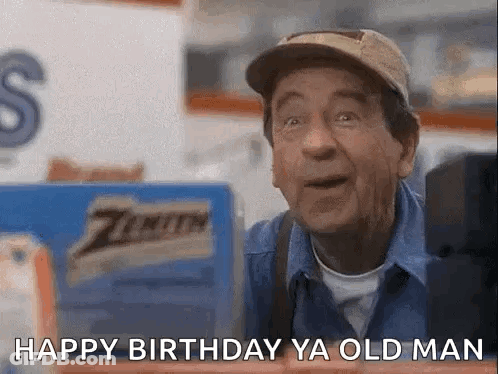 A Man Wearing A Hat And A Blue Shirt Is Standing In Front Of A Sign That Says Happy Birthday Ya Old Man . GIF