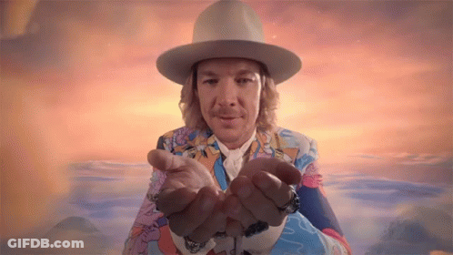A Man Wearing A Hat And A Colorful Suit Is Holding His Hands Out GIF