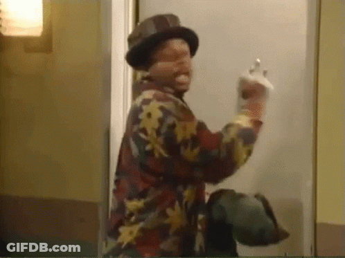 A Man Wearing A Hat And A Floral Shirt Is Standing In Front Of A Door And Giving The Middle Finger . GIF