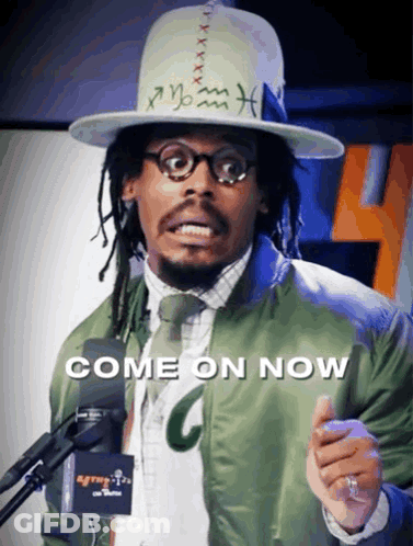 A Man Wearing A Hat And A Green Jacket Stands In Front Of A Microphone With The Words Come On Now On The Bottom GIF