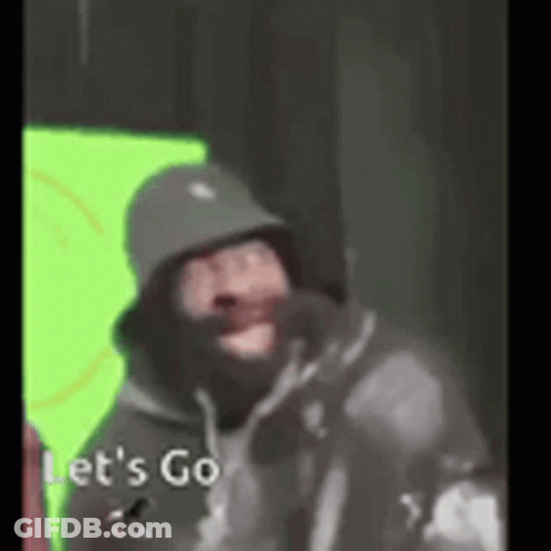 A Man Wearing A Hat And A Hoodie Is Standing In Front Of A Green Screen . GIF