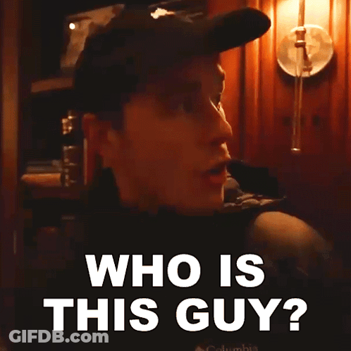 A Man Wearing A Hat And A Jacket Is Asking Who Is This Guy GIF