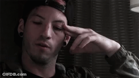 A Man Wearing A Hat And A Jacket Is Holding His Hand To His Forehead . GIF