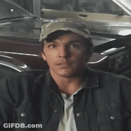 A Man Wearing A Hat And A Jacket Stands In Front Of A Parked Car GIF