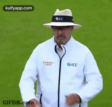 A Man Wearing A Hat And A Jacket That Says Emirates Fly Better Is Standing On A Field . GIF