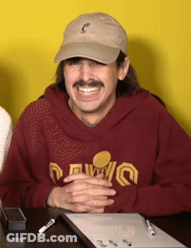 A Man Wearing A Hat And A Maroon Sweatshirt That Says ' Cleveland ' On It Sits At A Desk GIF