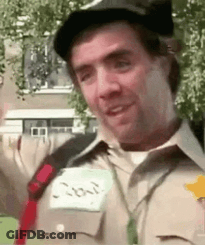 A Man Wearing A Hat And A Name Tag Is Smiling And Looking At The Camera . GIF