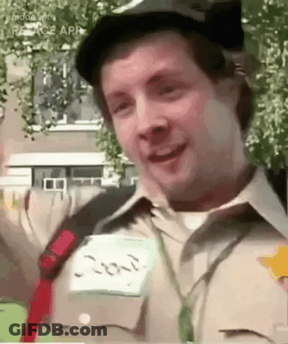 A Man Wearing A Hat And A Name Tag Is Smiling And Waving At The Camera . GIF