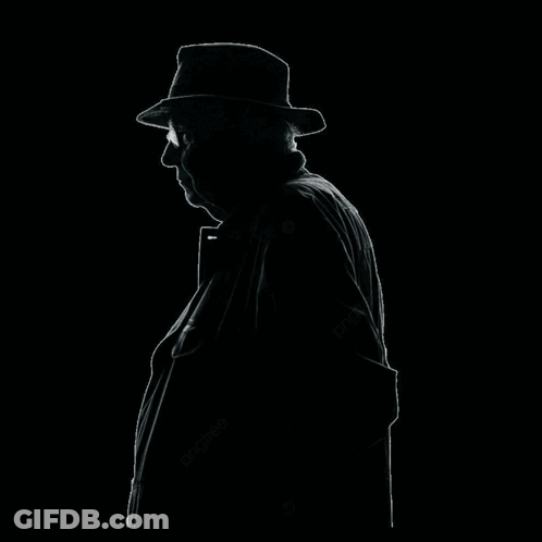 A Man Wearing A Hat And A Necklace Covering His Face With His Hand GIF