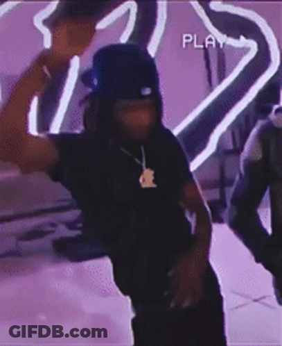 A Man Wearing A Hat And A Necklace Is Dancing In Front Of A Purple Background . GIF