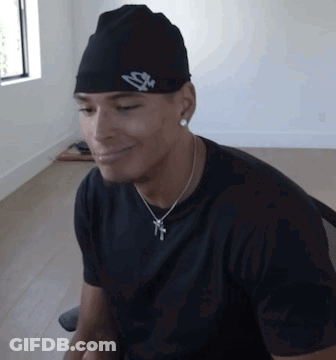 A Man Wearing A Hat And A Necklace Is Smiling GIF