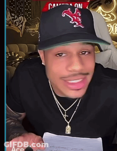 A Man Wearing A Hat And A Necklace Is Smiling GIF