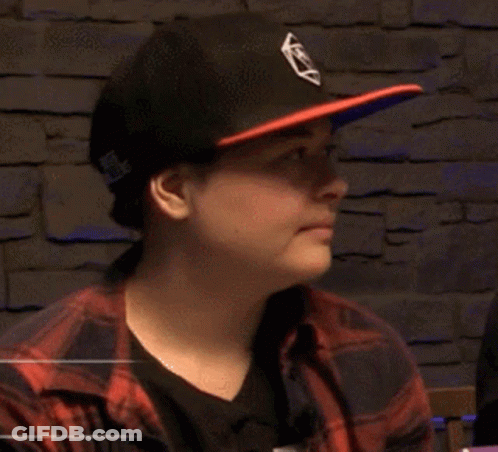 A Man Wearing A Hat And A Plaid Shirt Is Reading A Book And Smiling . GIF