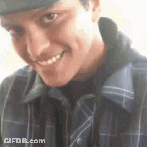 A Man Wearing A Hat And A Plaid Shirt Is Smiling For The Camera . GIF