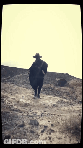 Man In Hat And Poncho Walking On Dirt Road GIF