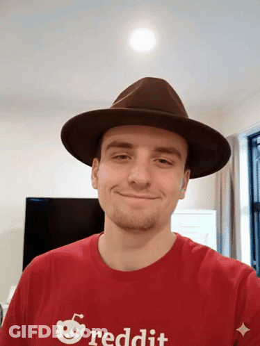 A Man Wearing A Hat And A Reddit Shirt Smiles For The Camera GIF