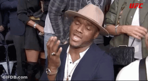 A Man Wearing A Hat And A Ring Is Sitting In A Crowd Of People . GIF