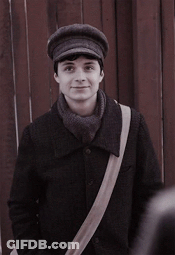 A Man Wearing A Hat And A Scarf Is Standing In Front Of A Wooden Fence GIF
