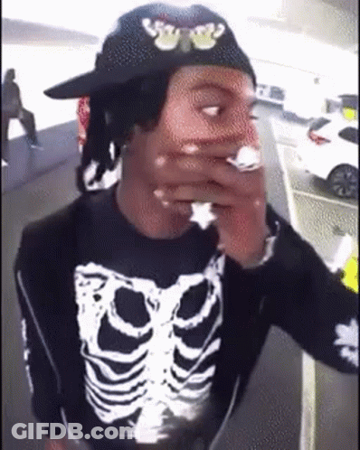 A Man Wearing A Hat And A Skeleton Shirt Is Smoking A Cigarette . GIF