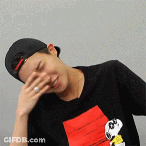 A Man Wearing A Hat And A Snoopy Shirt Covering His Face With His Hand . GIF