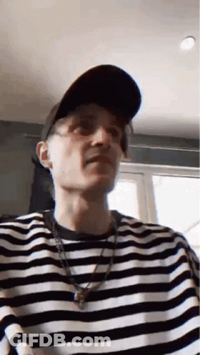 A Man Wearing A Hat And A Striped Shirt Is Making A Face . GIF