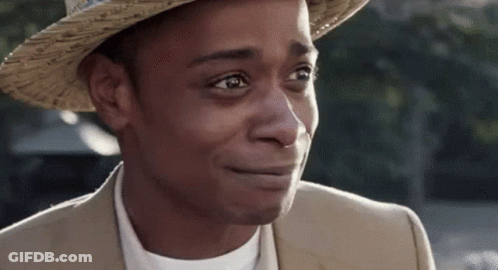A Man Wearing A Hat And A Suit Is Smiling And Looking At The Camera . GIF