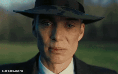 A Man Wearing A Hat And A Suit Looks At The Camera GIF