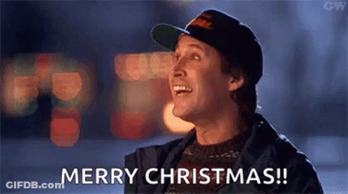 A Man Wearing A Hat And A Sweater Is Laughing And Saying Merry Christmas . GIF