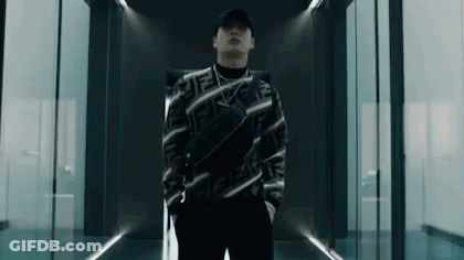 A Man Wearing A Hat And A Sweater Is Standing In A Hallway . GIF