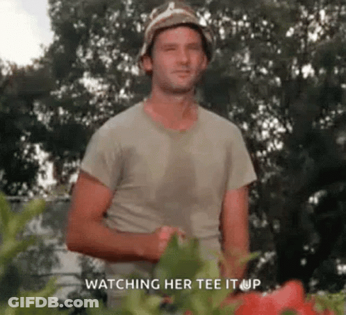 A Man Wearing A Hat And A T-Shirt Is Standing In Front Of A Garden . GIF