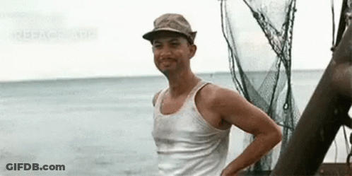 A Man Wearing A Hat And A Tank Top Is Standing On A Boat Near The Ocean . GIF