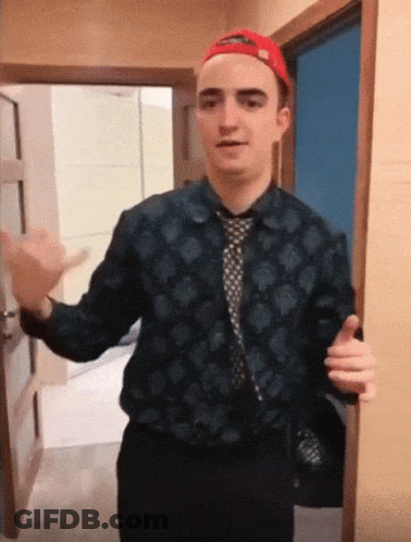 A Man Wearing A Hat And A Tie Is Standing In A Doorway GIF