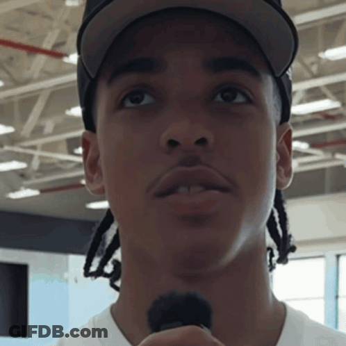 A Man Wearing A Hat And A White Shirt Holds A Microphone In His Hand GIF