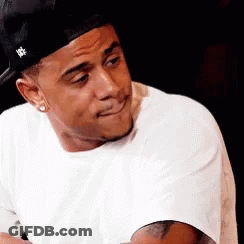 A Man Wearing A Hat And A White Shirt Is Making A Funny Face GIF