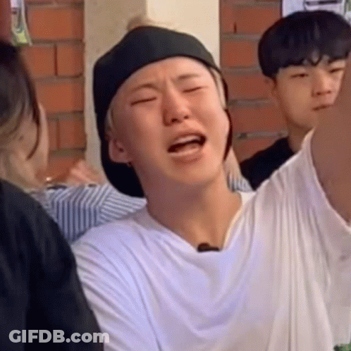 A Man Wearing A Hat And A White Shirt Is Making A Funny Face While Sitting In A Crowd . GIF