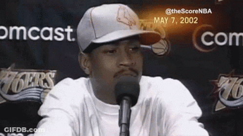 A Man Wearing A Hat And A White Shirt Is Talking Into A Microphone . GIF