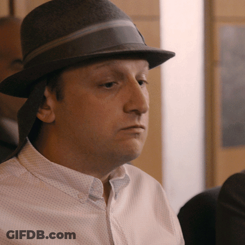 A Man Wearing A Hat And A White Shirt Looks To The Side GIF