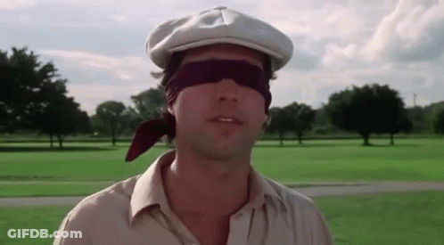 A Man Wearing A Hat And Blindfold Is Standing In A Field . GIF