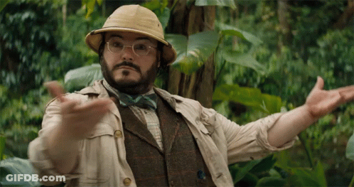 A Man Wearing A Hat And Bow Tie Is Standing In The Jungle GIF