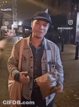 A Man Wearing A Hat And Carrying A Bag Is Standing On A Street With The Hashtag @Emperorgreep GIF