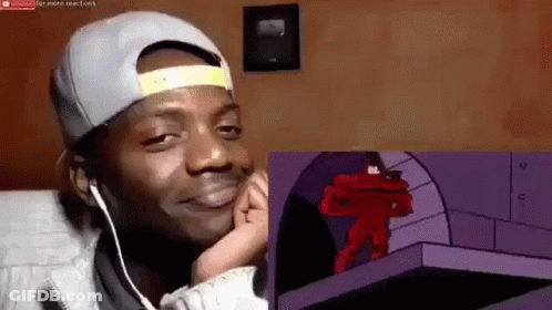 A Man Wearing A Hat And Ear Buds Is Watching A Cartoon And Making A Funny Face GIF