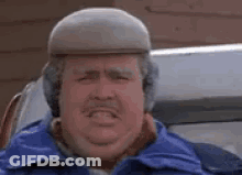 A Man Wearing A Hat And Ear Muffs Is Making A Funny Face While Sitting In A Car . GIF