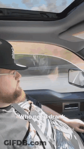 A Man Wearing A Hat And Glasses Is Driving A Car With The Words Who Needs Drank Below Him GIF