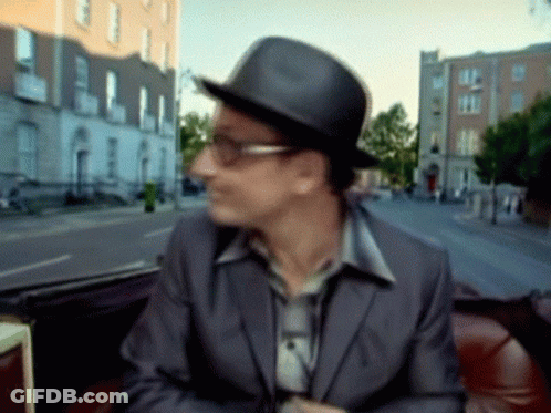 A Man Wearing A Hat And Glasses Is Sitting In Front Of A Blurry Street GIF