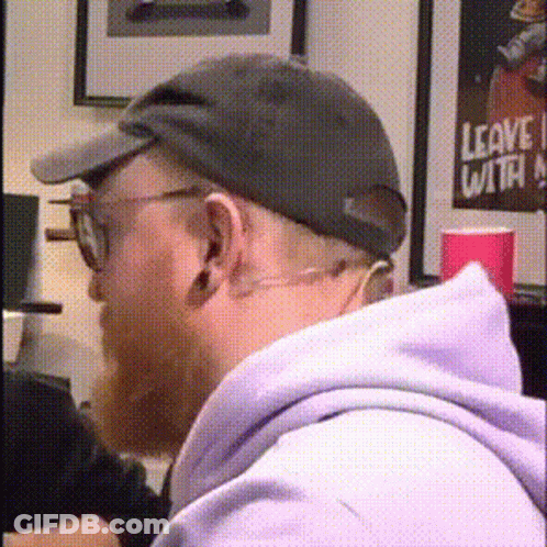 A Man Wearing A Hat And Glasses Is Sitting In Front Of A Leave With Poster GIF