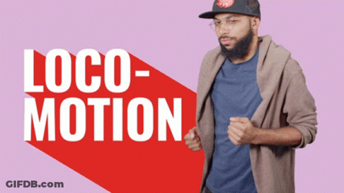 A Man Wearing A Hat And Glasses Is Standing In Front Of A Sign That Says Loco Motion GIF