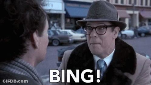 A Man Wearing A Hat And Glasses Is Talking To Another Man On A City Street . GIF