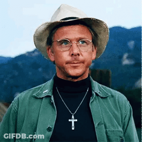 A Man Wearing A Hat And Glasses Is Wearing A Necklace With A Cross Pendant . GIF