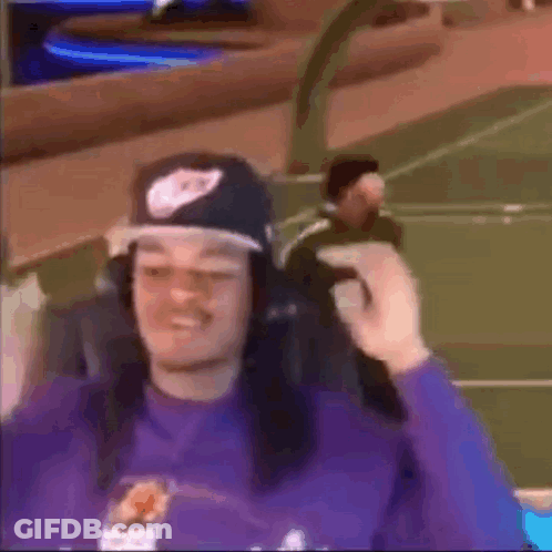 A Man Wearing A Hat And Headphones Is Sitting In A Chair On A Basketball Court . GIF