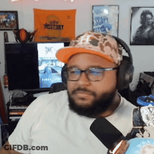 A Man Wearing A Hat And Headphones Is Sitting In Front Of A Sign That Says Escape Kit GIF